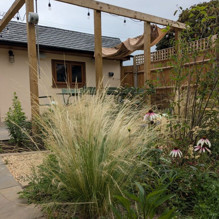 Stipa tenuissima in a garden with seating area beyond.